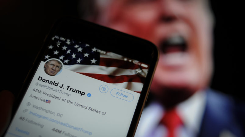The Twitter app is seen with an image of US president Donald Trump in the background in this